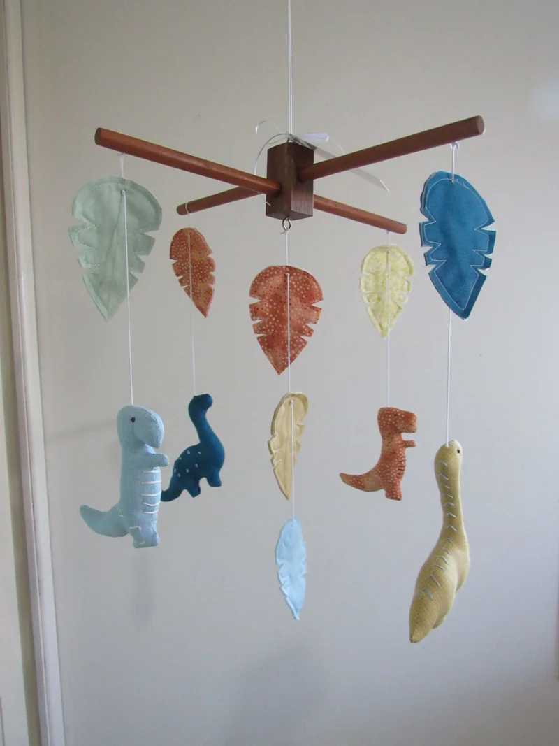 Móbile com dinossauros azuis, amarelos e laranja e folhas coloridas.