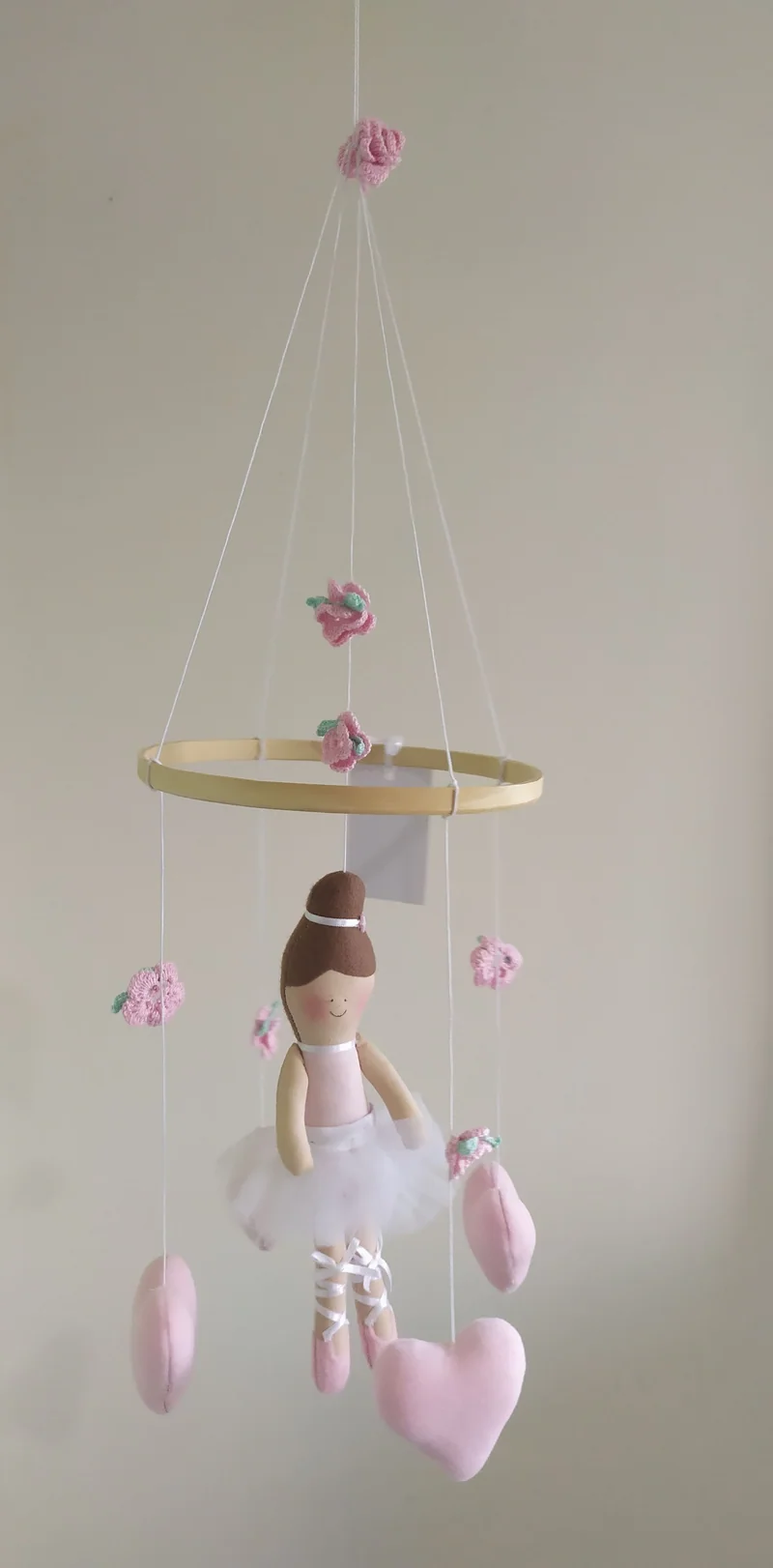 Fada de vestido rosa e asas brancas, pendurada em um aro pequeno, com corações de tecido rosa abaixo dela.