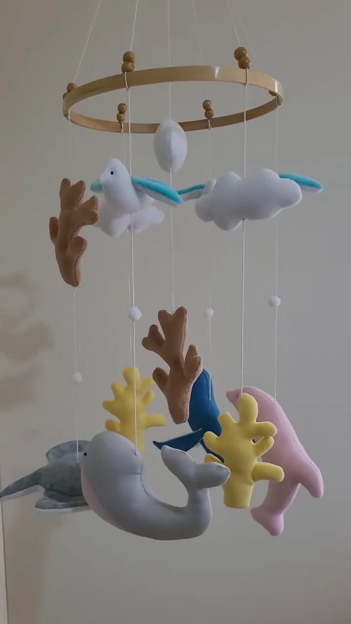 Móbile com animais marinhos, nuvens e elementos de tecido suspensos em um aro.