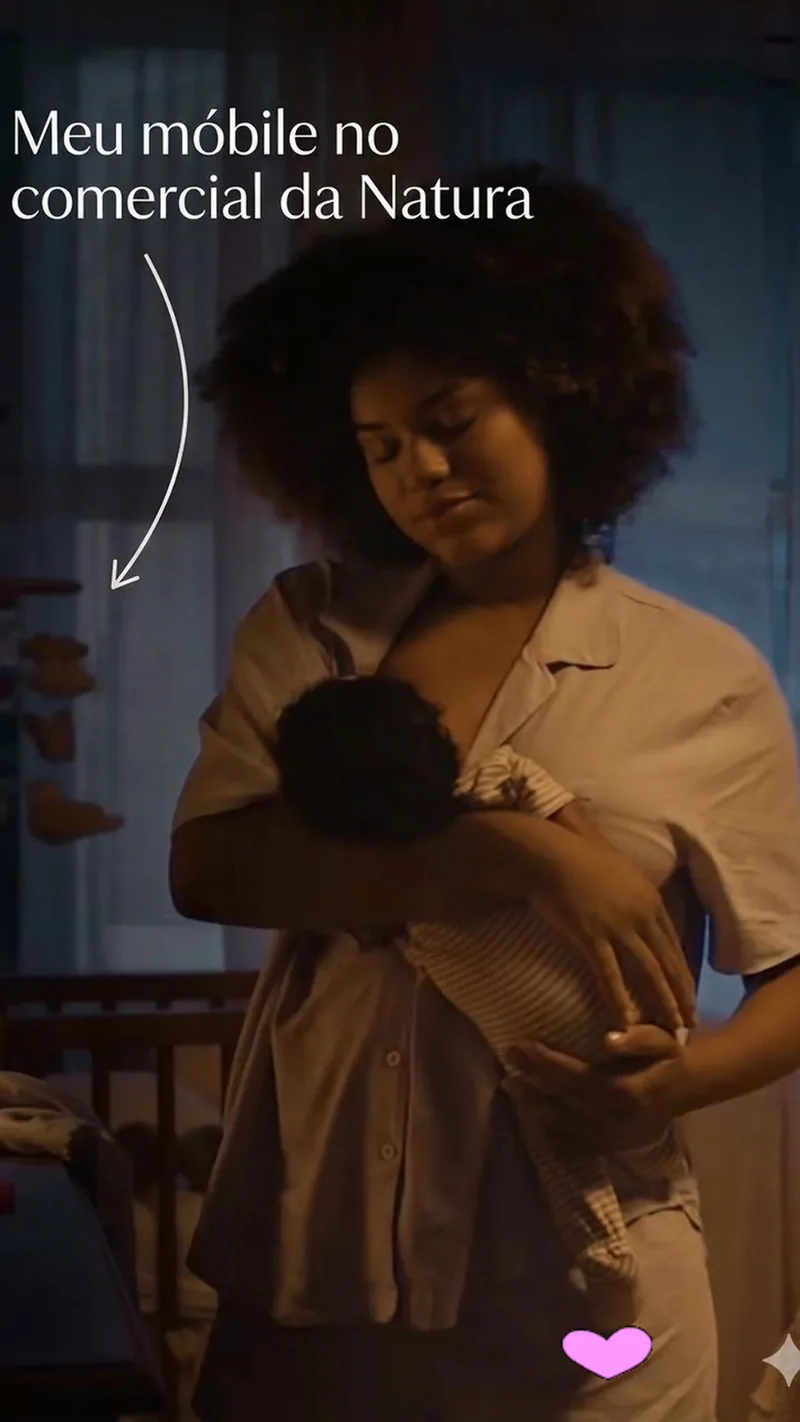Trecho do comercial da Natura: uma mãe segura o bebê no colo, com um móbile do atelier pendurado ao fundo e a legenda de Maria Silvia.