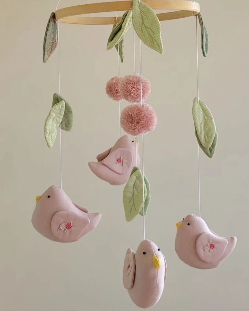 Móbile com pássaros rosa, folhas verdes e pequenas bolas de tecido.