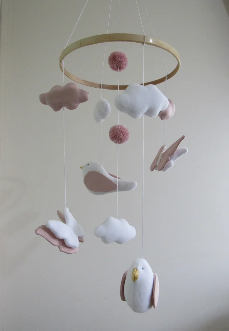 Móbile em aro de madeira com pássaros, borboletas e nuvens em rosa e branco.