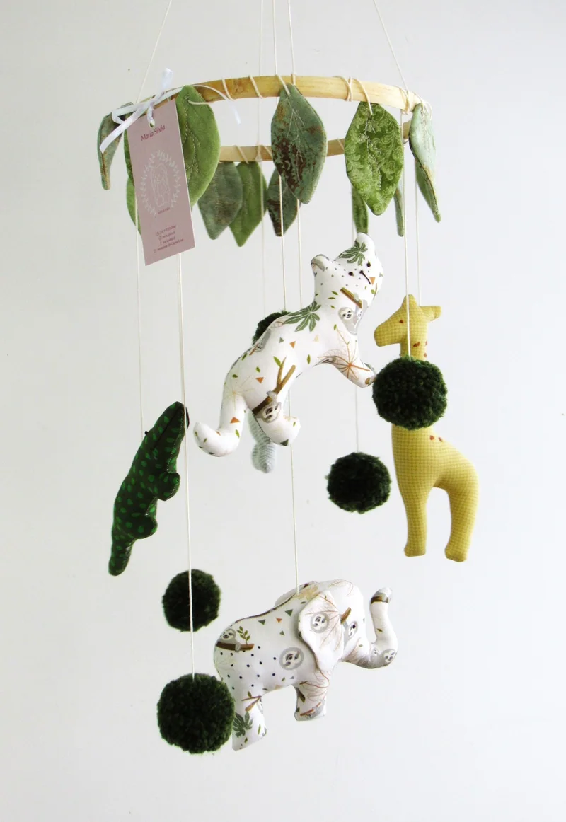Móbile com girafa, zebra, elefante e folhas verdes de tecido.