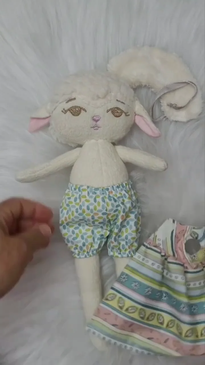 Ovelhinha de tecido branco com roupa estampada sendo mostrada pelas mãos da artesã.