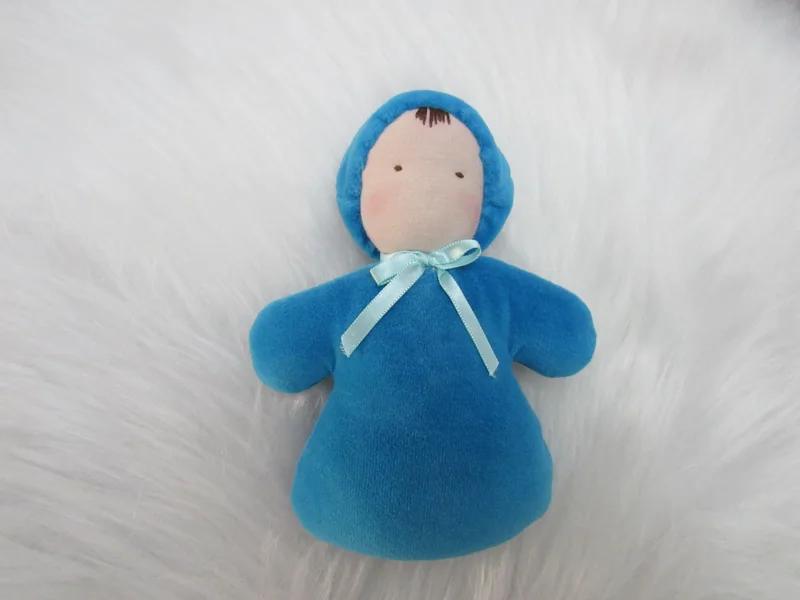 Naninha de capuz azul e laço branco sobre fundo claro.