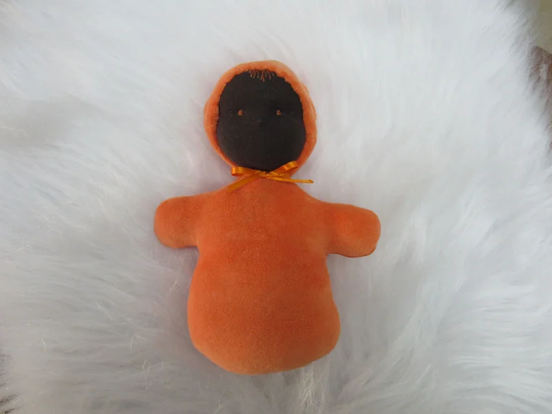 Naninha de pele escura com capuz e roupa laranja.