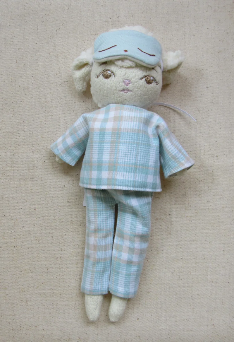 Ovelhinha de pijama xadrez azul-claro com máscara de dormir na testa.