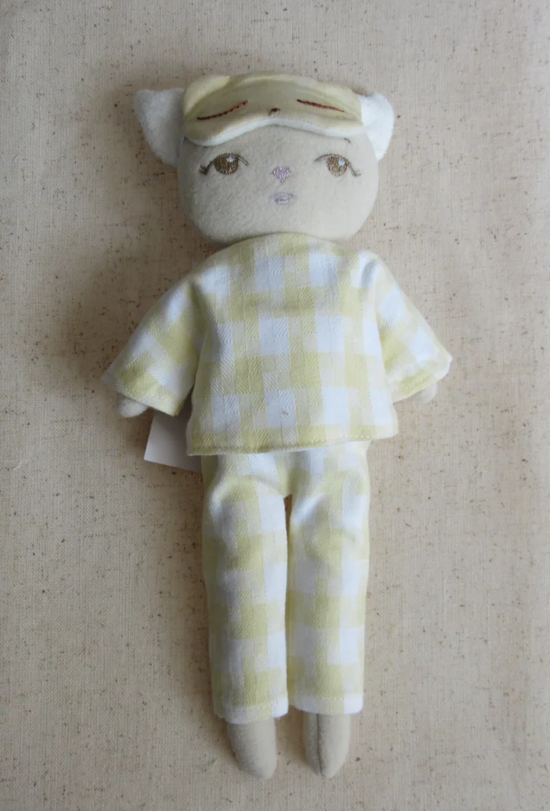 Gatinho claro com pijama xadrez amarelo e máscara na testa.