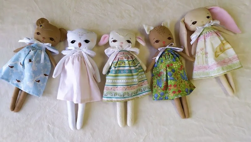 Cinco bichinhos de tecido com vestidos em azul, rosa, verde e amarelo.