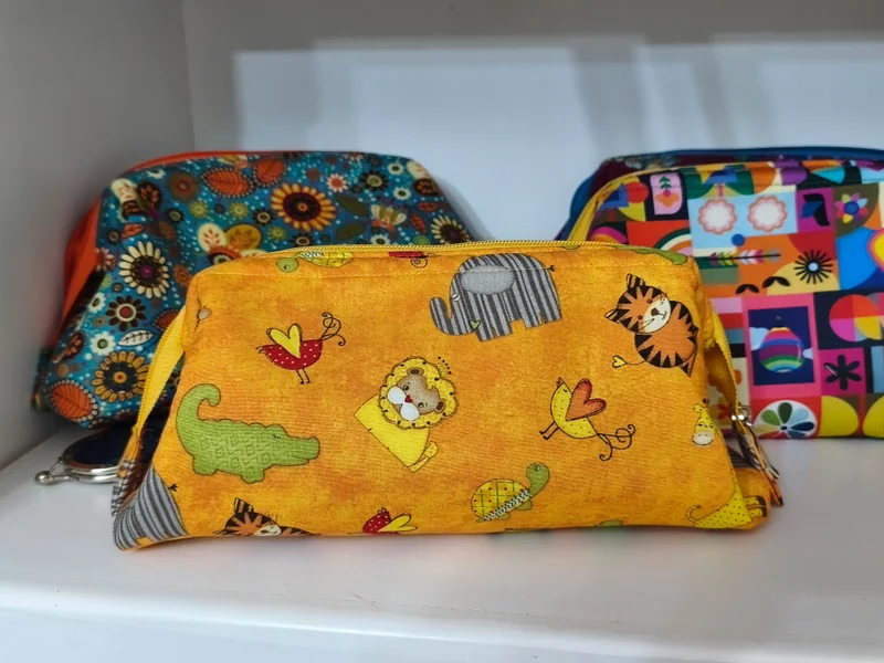 Nécessaire amarela com bichos estampados, ao lado de outras nécessaires coloridas.