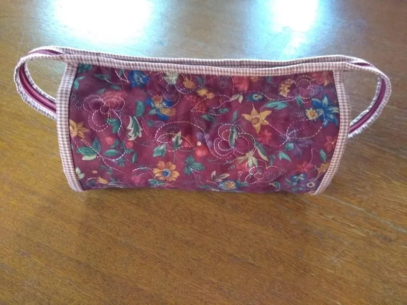 Vista externa da nécessaire com estampa floral e acabamento xadrez rosa.