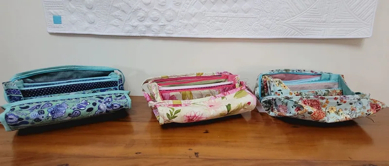 Três nécessaires com divisórias, em tecidos estampados, sobre a mesa.