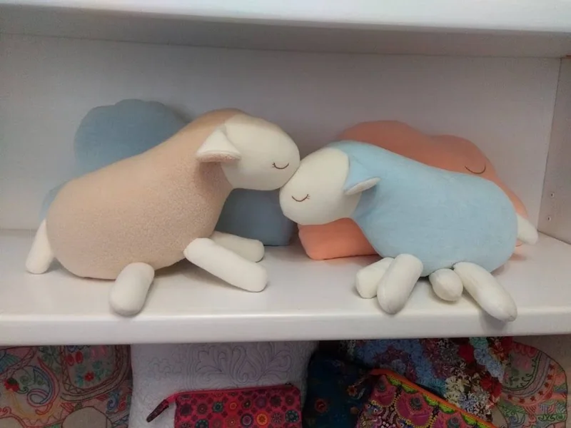 Ovelhinhas de tecido em rosa, azul e bege, deitadas lado a lado.