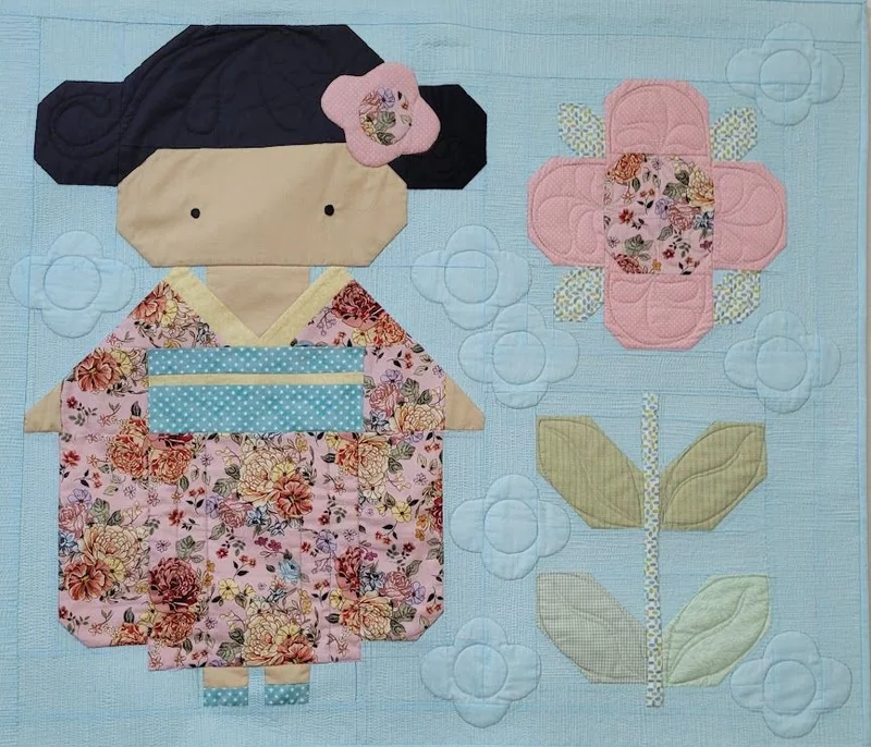 Painel azul com menina de vestido estampado e grande flor de tecido.