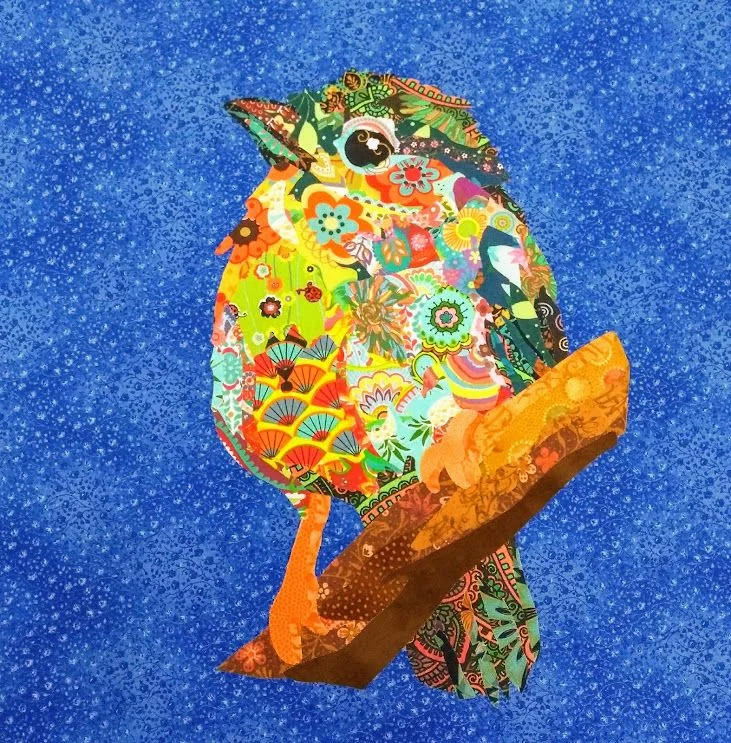 Passarinho feito de retalhos coloridos sobre tecido azul.