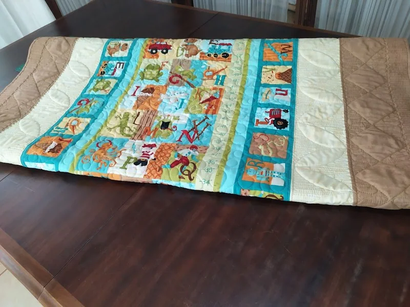 Peça de patchwork aberta sobre uma mesa, com bichos e molduras azuis e beges.