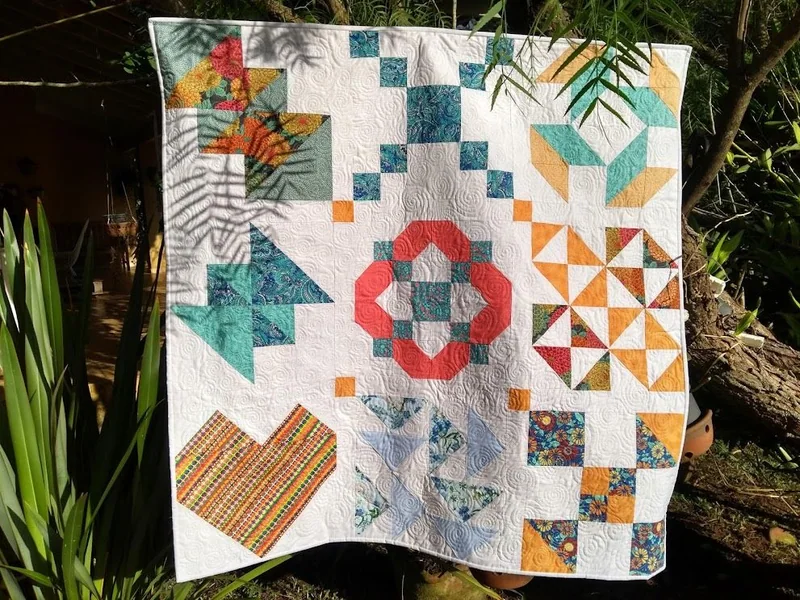 Peça de patchwork pendurada ao ar livre, com blocos geométricos coloridos.