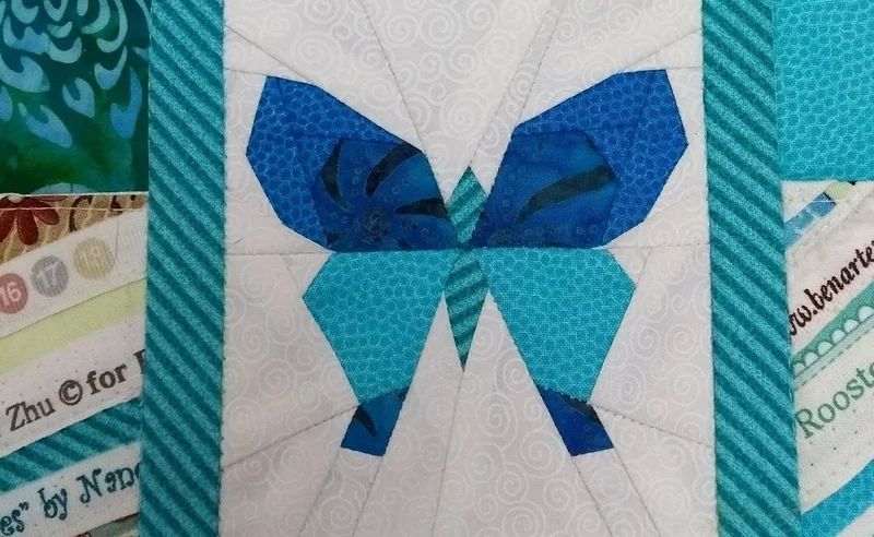 Detalhe de uma borboleta geométrica azul, cercada por molduras de tecido.