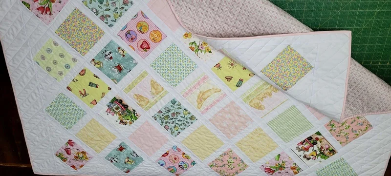 Patchwork de quadrados em rosa, verde e amarelo sobre tecidos claros.