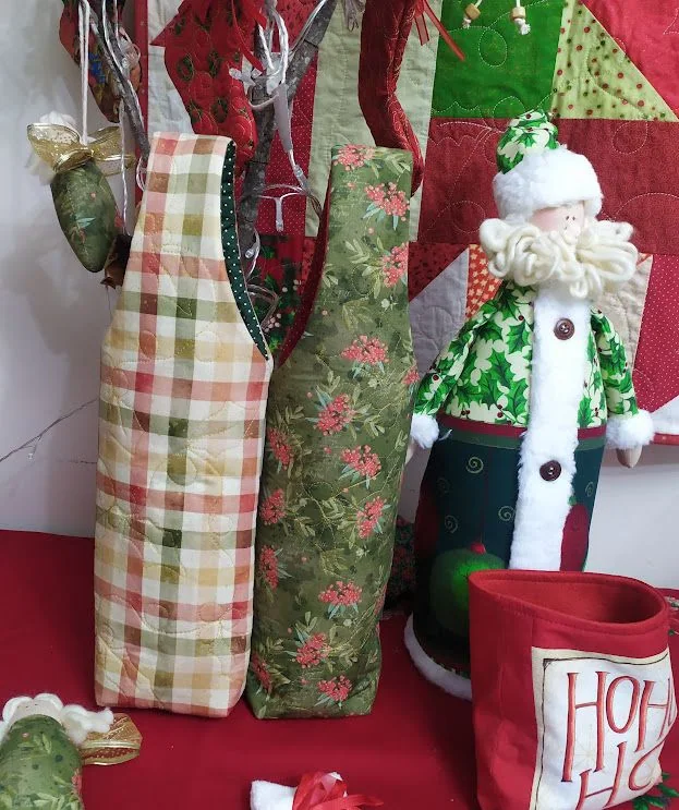 Dois porta-garrafas de tecido com alças, um xadrez e outro verde estampado.