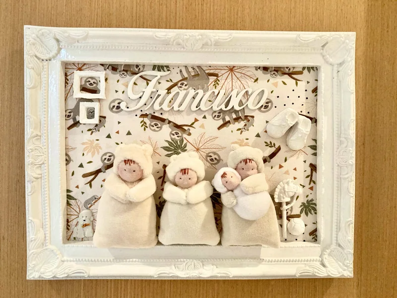Quadro de moldura clara com o nome Francisco e pequenos bonecos vestidos de branco.