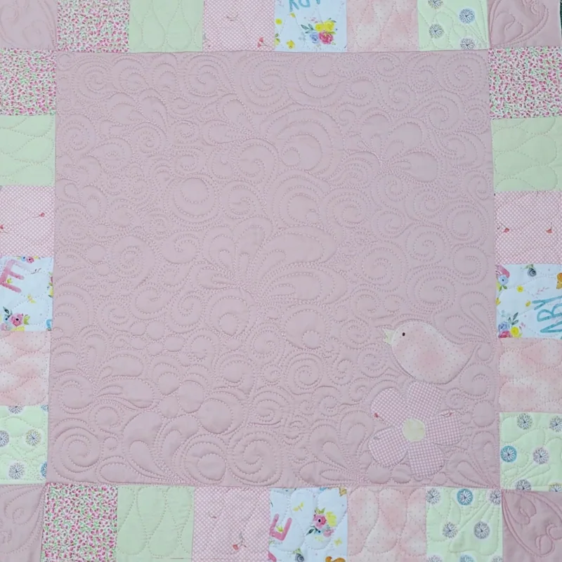 Almofada rosa com moldura de retalhos estampados, quilting e um pequeno pássaro.
