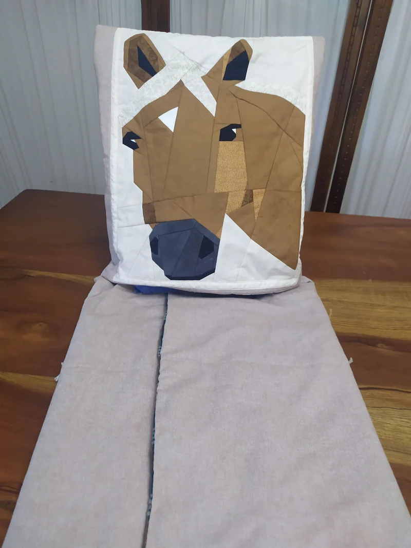 Quillow com a cabeça de um cavalo em patchwork, acompanhado da manta clara aberta.