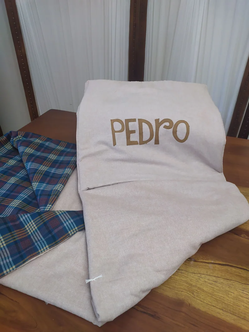 Manta clara com o nome Pedro bordado em tom marrom.