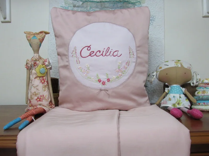 Quillow Cecília acompanhado da manta rosa aberta sobre a mesa.