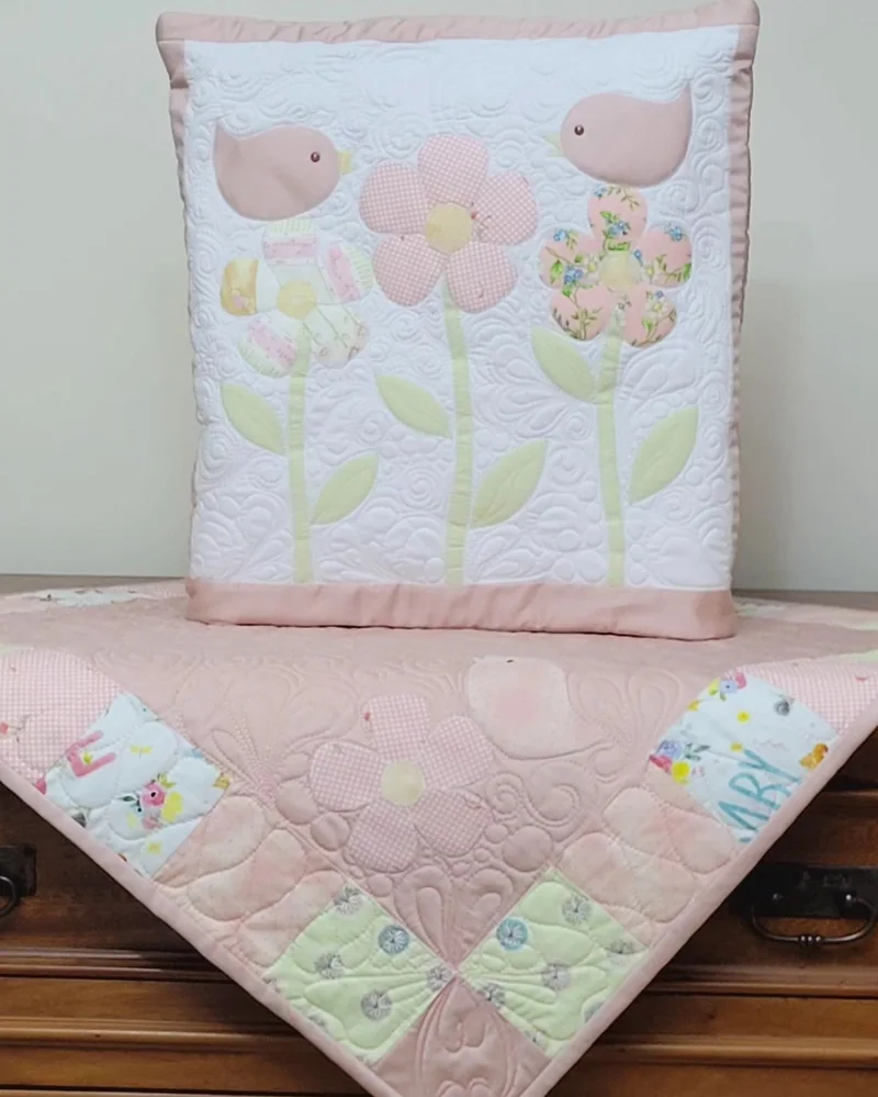Quillow e manta rosa com flores, pássaros e desenhos de quilting.