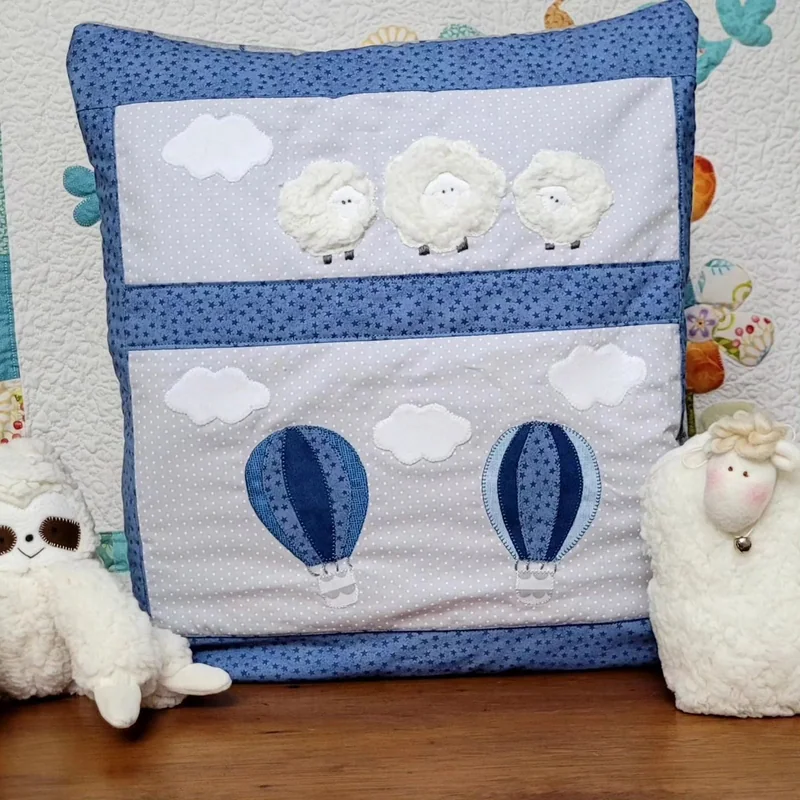 Quillow azul com balões e nuvens, acompanhado por ovelhinhas e elementos do conjunto.