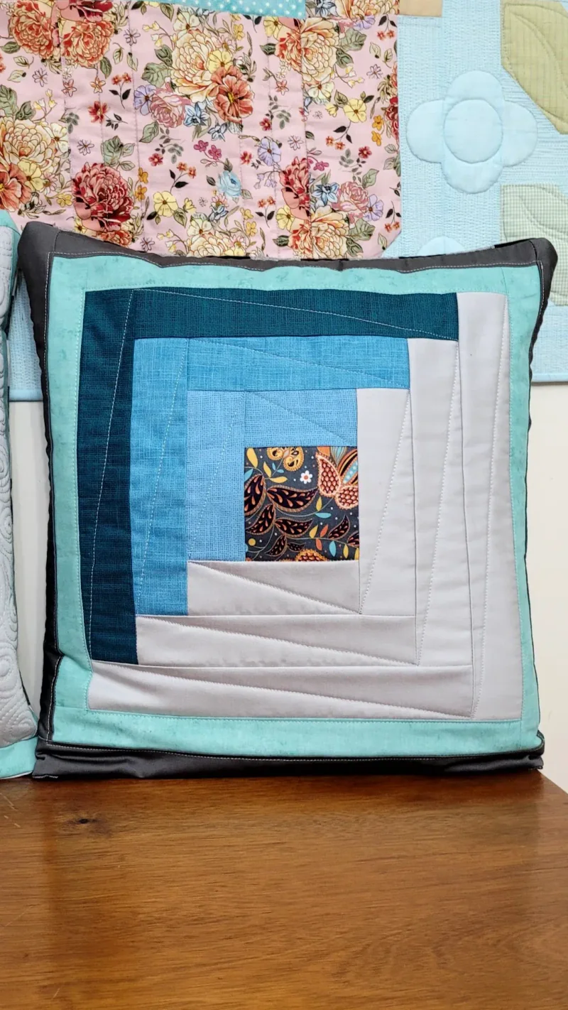 Almofada com blocos concêntricos em azul, branco e vinho, fotografada no mesmo conjunto.