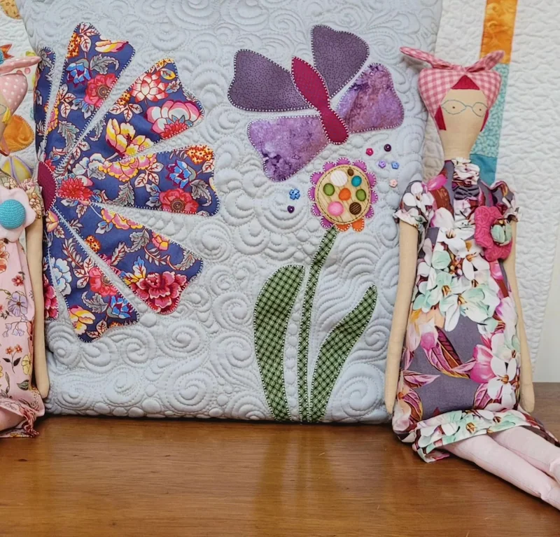 Quillow com flores e borboleta em patchwork ao lado de uma boneca Tilda.