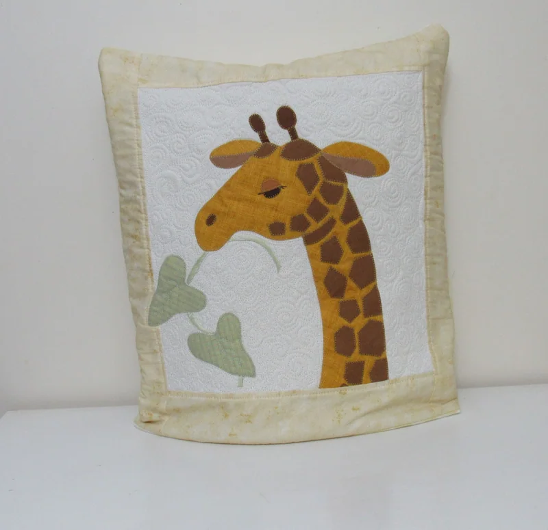 Quillow claro com uma girafa amarela e folhas verdes aplicadas em tecido.