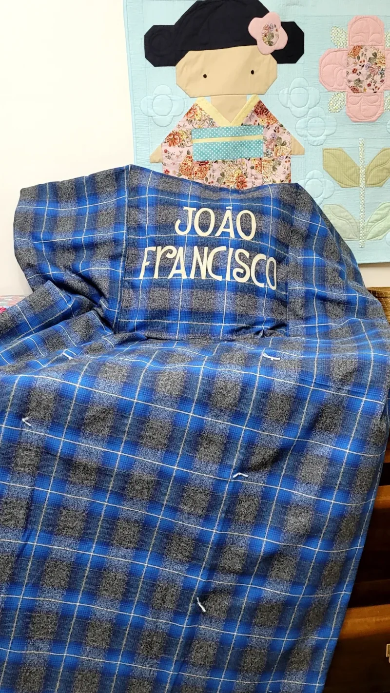 Manta xadrez azul aberta sobre a cadeira, com o nome João Francisco bordado.