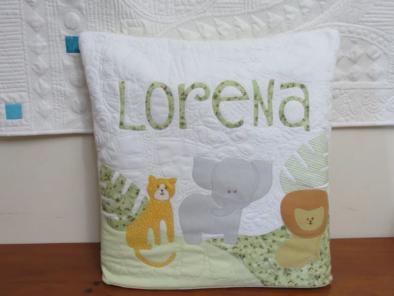 Quillow com o nome Lorena, girafa, elefante e leão sobre tecido claro.