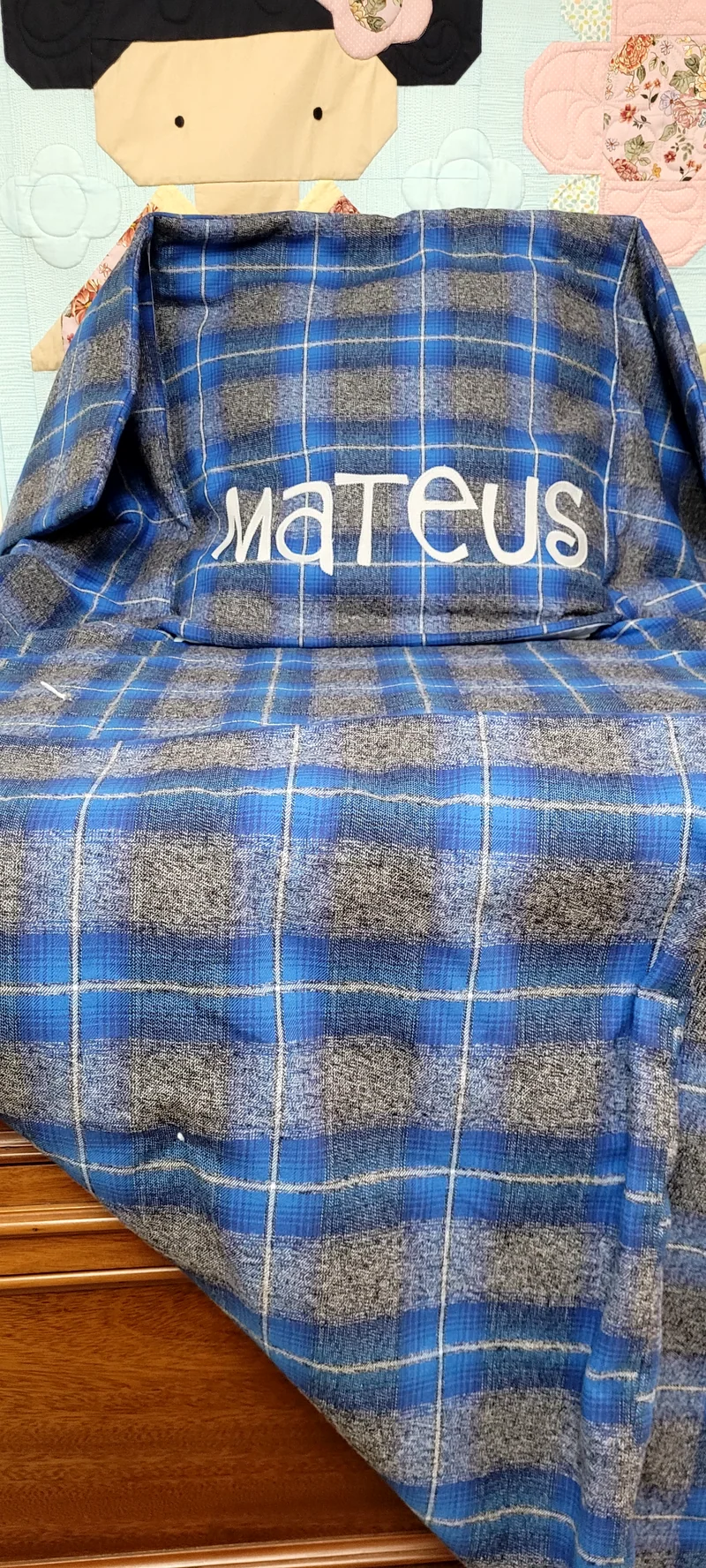 Manta xadrez azul e cinza aberta sobre a cadeira, com o nome Mateus bordado.