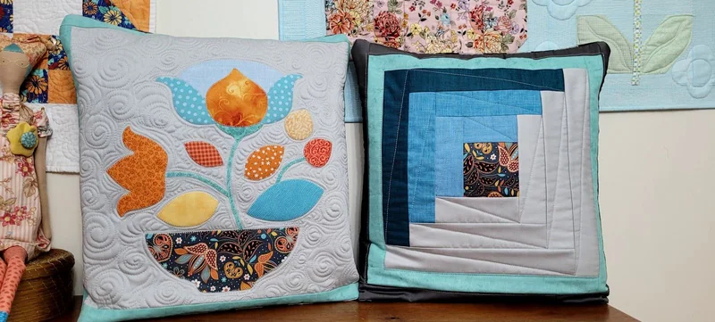 Quillow com flores aplicadas ao lado de outro de blocos geométricos azuis.