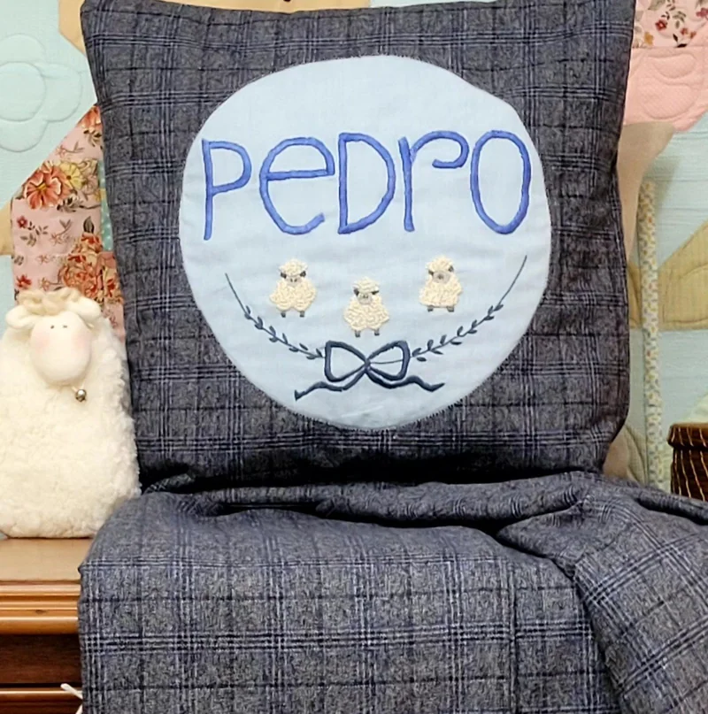Quillow cinza com o nome Pedro em azul e ovelhinhas bordadas.