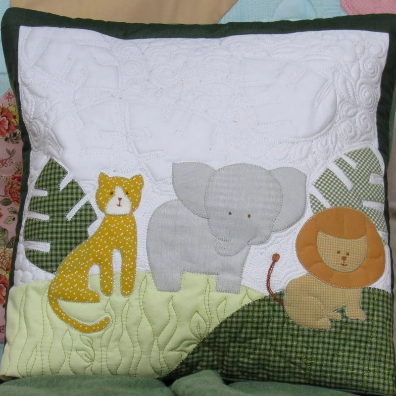 Quillow com leão, elefante e girafa sobre tecido verde.