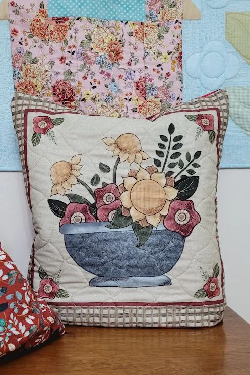 Quillow com um vaso de flores aplicado sobre fundo claro.