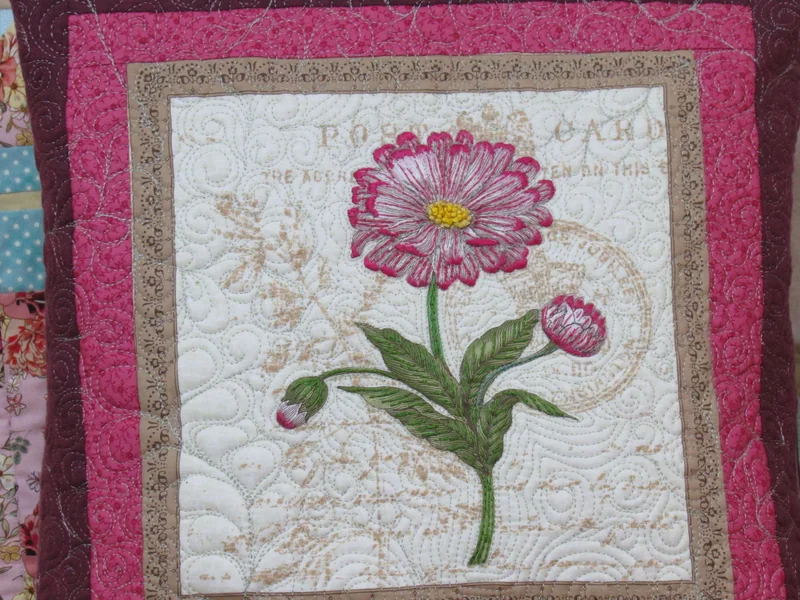 Detalhe da flor rosa, das folhas e do quilting no tecido claro.