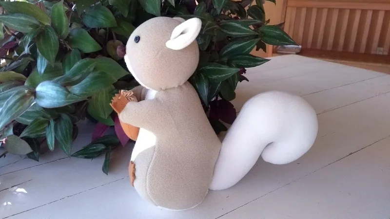 Esquilo de tecido marrom e branco segurando uma pequena peça entre as patas.