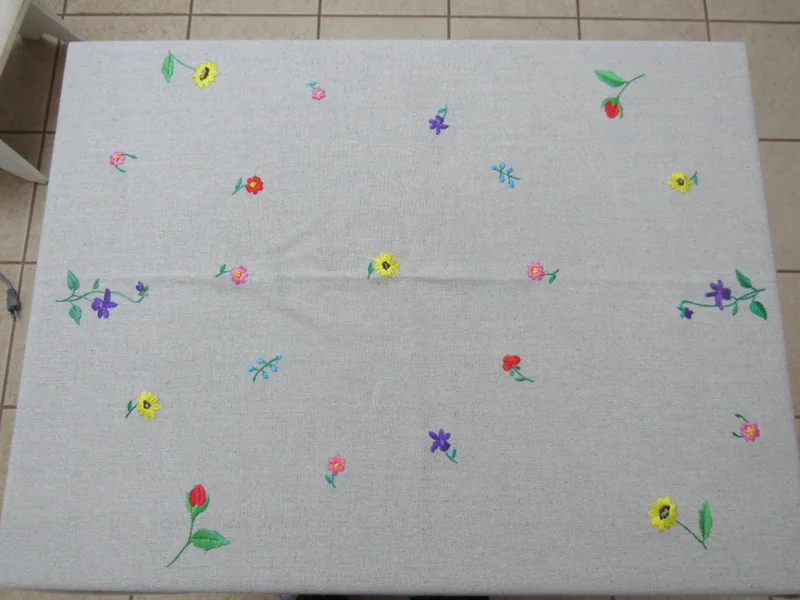 Toalha clara aberta sobre uma mesa, com pequenas flores coloridas bordadas.