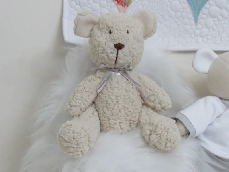 Urso claro de tecido texturizado com um laço no pescoço.