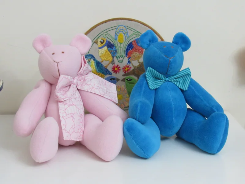 Urso rosa e urso azul sentados lado a lado.